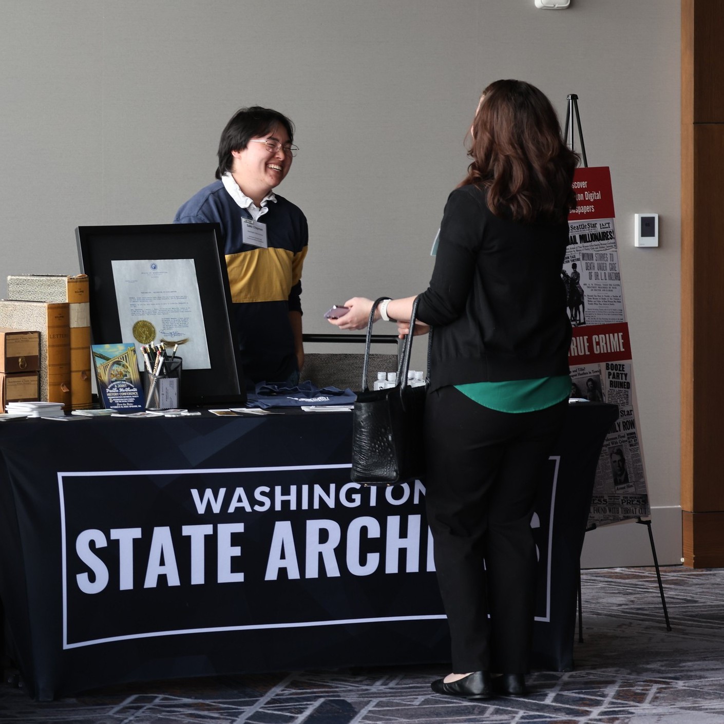 State archives employee tabling at an event engaged in conversation with a visitor.